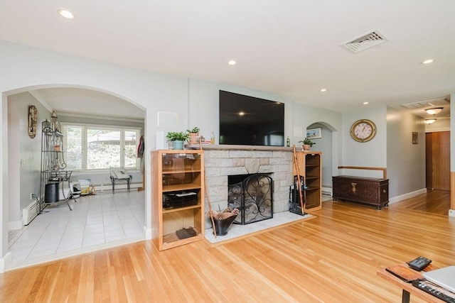 35 Williams St, Lincoln, RI 02865 - living room with baseboards, arched walkways, a baseboard heating unit, a stone fireplace, and wood finished floors