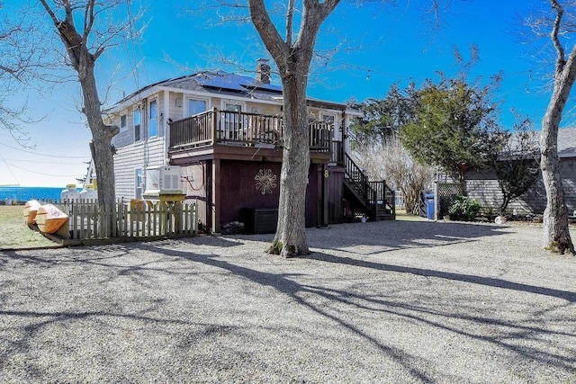 back of property with roof mounted solar panels, fence, stairway, and a wooden deck