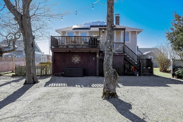 back of property featuring a chimney, solar panels, fence, a deck, and stairs