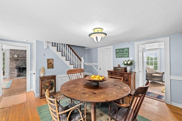 146 Chief Justic Cushing Hwy, Scituate, MA 02066 - dining room featuring stairs, light wood-style flooring, a brick fireplace, and a textured ceiling