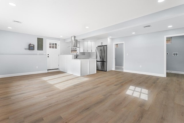 kitchen with wall chimney exhaust hood, light hardwood / wood-style flooring, stainless steel refrigerator, and white cabinets