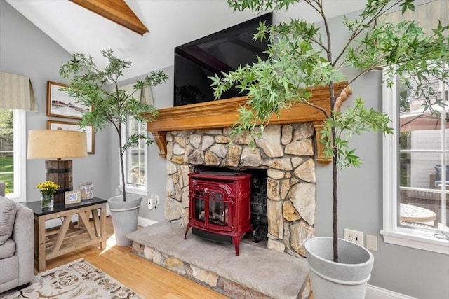 sitting room with vaulted ceiling, baseboards, a wood stove, and wood finished floors