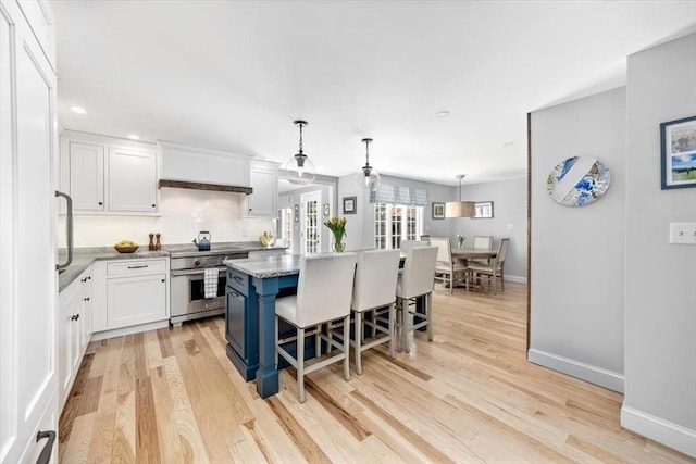 kitchen with a breakfast bar, high end stainless steel range, light wood finished floors, white cabinetry, and baseboards
