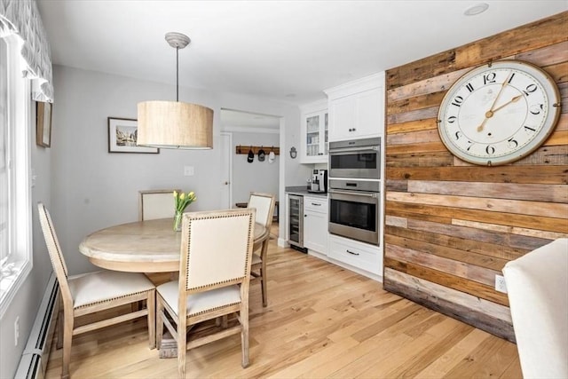 kitchen with wine cooler, baseboard heating, stainless steel double oven, white cabinets, and light wood finished floors