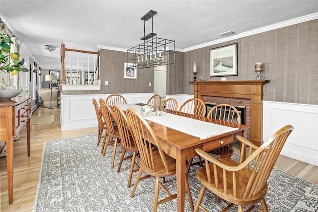dining area featuring light wood-style floors, a wainscoted wall, crown molding, and visible vents