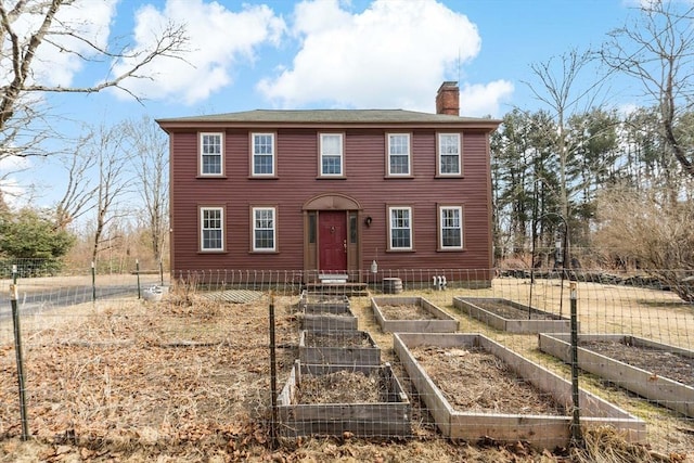 view of front of house featuring a chimney, fence, and a garden