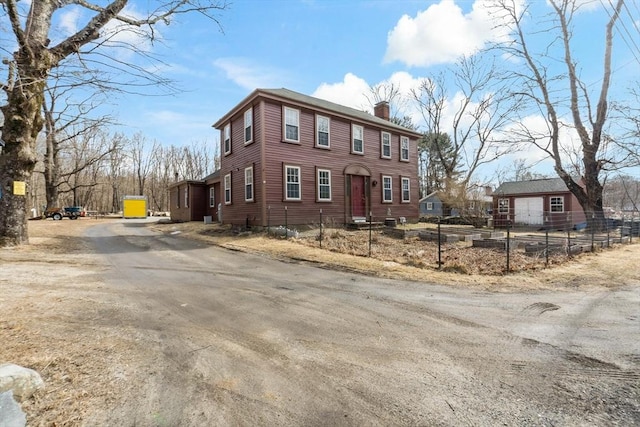 view of front of home featuring an outbuilding, a chimney, driveway, and fence