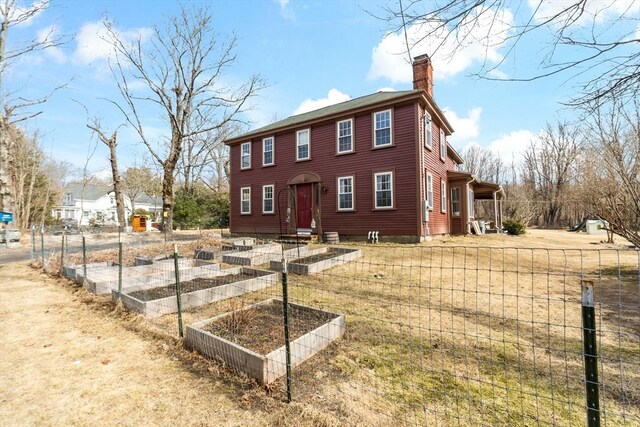 colonial house featuring a garden, fence, and a chimney