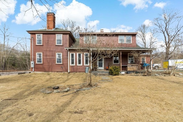 rear view of property with a porch, a yard, and a chimney