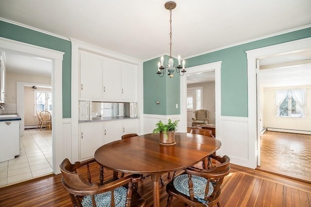 dining area with an inviting chandelier, a baseboard heating unit, crown molding, and sink