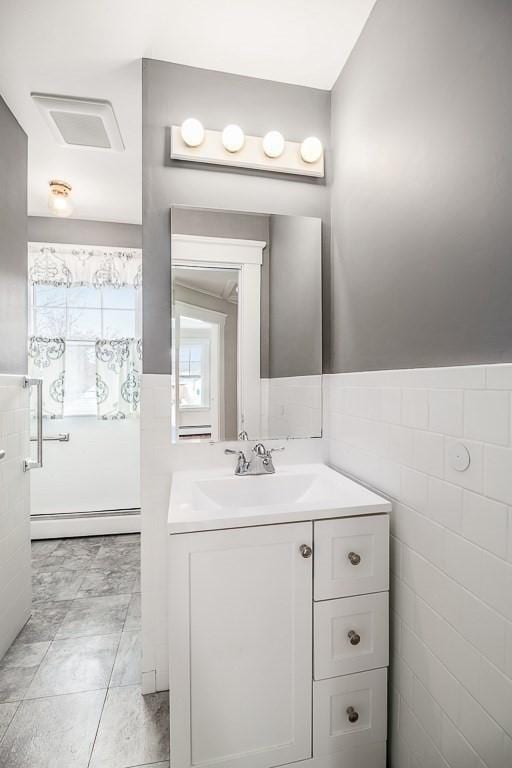 bathroom with a baseboard radiator, vanity, and tile walls