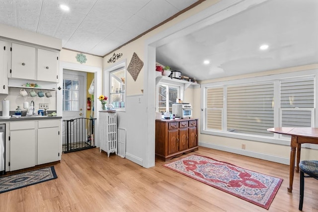 kitchen with white cabinets, light wood-type flooring, radiator, and sink