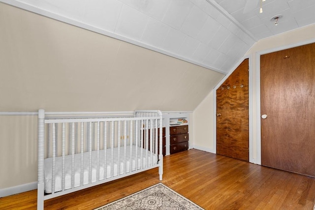 unfurnished bedroom featuring lofted ceiling, hardwood / wood-style flooring, and a nursery area