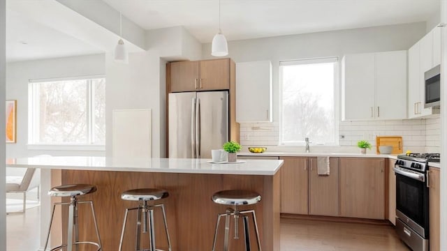 kitchen featuring white cabinets, appliances with stainless steel finishes, a center island, light countertops, and pendant lighting