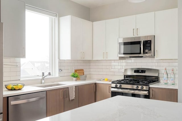 kitchen with stainless steel appliances, light countertops, white cabinetry, and a sink