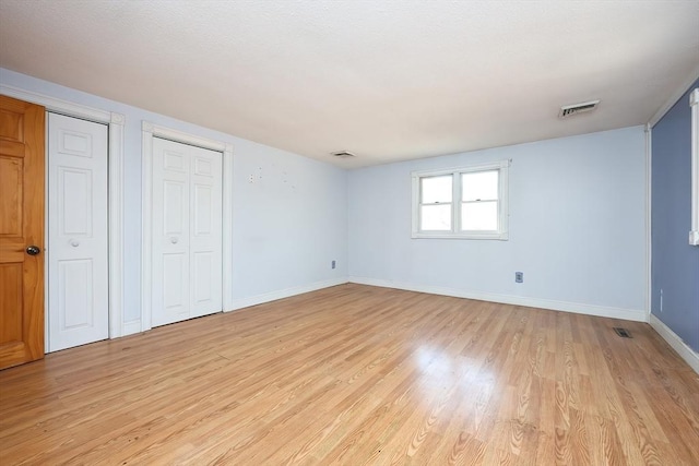 unfurnished bedroom featuring light hardwood / wood-style floors and two closets