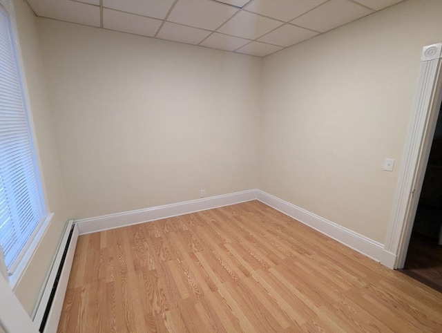 spare room with a drop ceiling, baseboard heating, light wood-type flooring, and baseboards