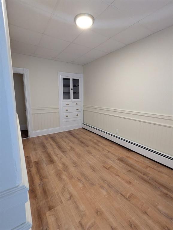 empty room featuring a wainscoted wall, a drop ceiling, baseboard heating, and wood finished floors