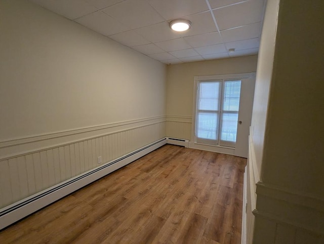 unfurnished room featuring a baseboard heating unit, wainscoting, a drop ceiling, and light wood-style flooring