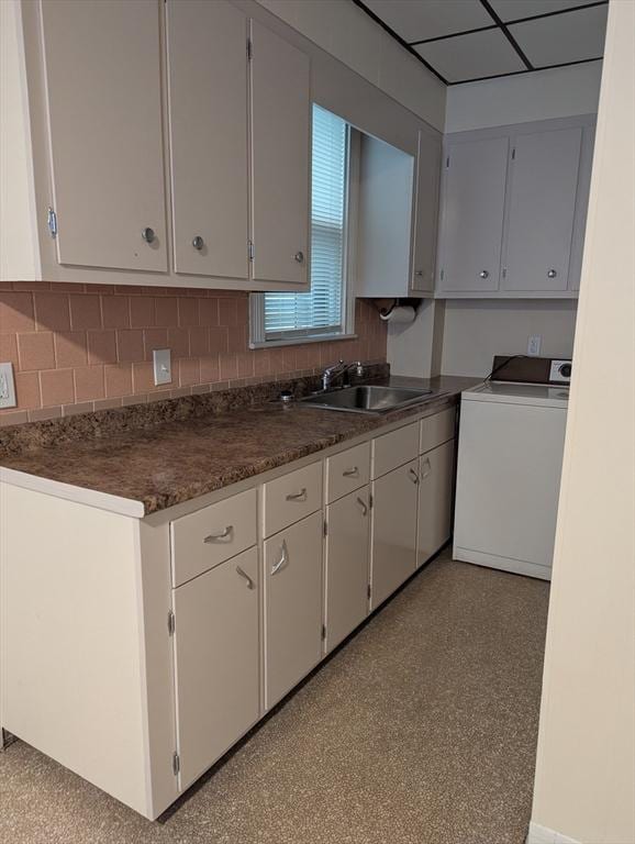 kitchen featuring a sink, white cabinets, decorative backsplash, washer / clothes dryer, and dark countertops