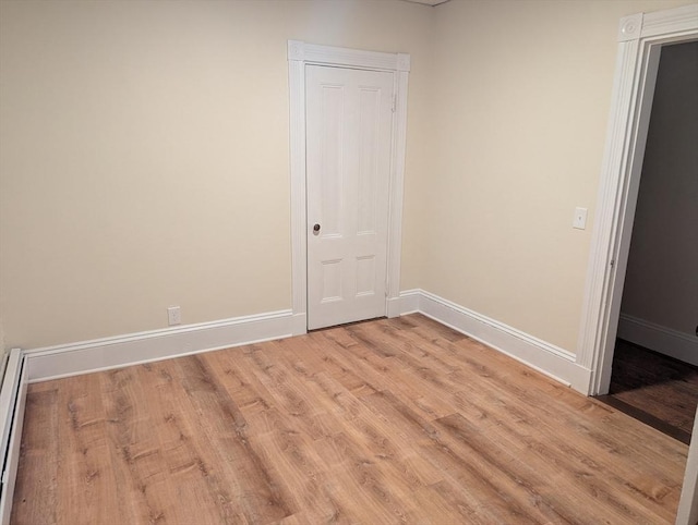 empty room featuring light wood-style floors, baseboards, and a baseboard heating unit