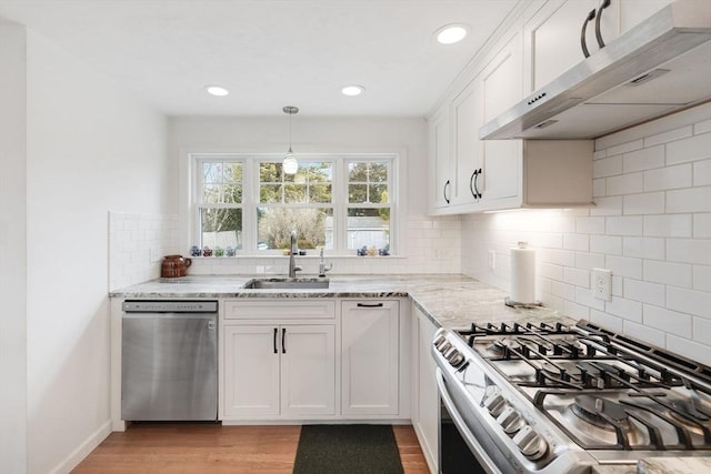 kitchen featuring light stone counters, range hood, stainless steel appliances, white cabinetry, and a sink