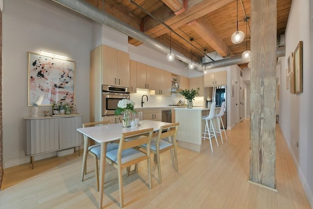 kitchen featuring light wood-style flooring, appliances with stainless steel finishes, a high ceiling, light brown cabinetry, and a sink