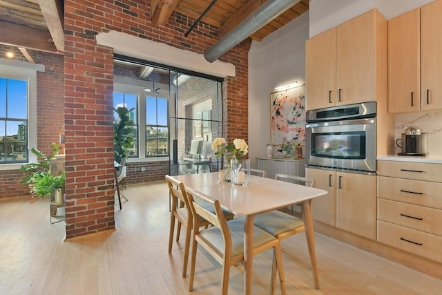 kitchen featuring plenty of natural light, brick wall, beamed ceiling, light brown cabinetry, and stainless steel oven