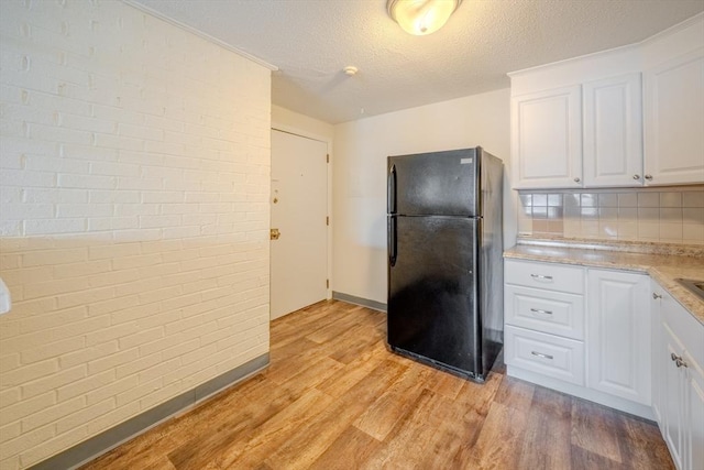 kitchen with black fridge, a textured ceiling, light hardwood / wood-style flooring, brick wall, and white cabinets