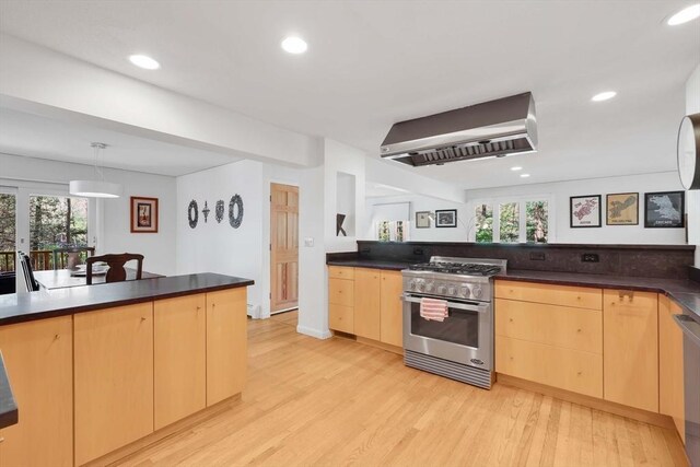 kitchen with wall chimney range hood, light brown cabinetry, dark countertops, light wood-style floors, and stainless steel appliances