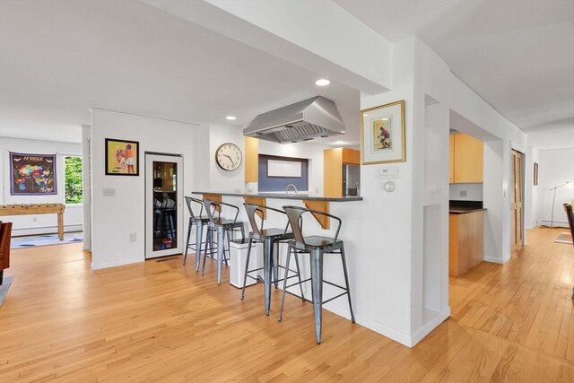 kitchen featuring baseboards, ventilation hood, stainless steel fridge, a breakfast bar, and light wood-style flooring