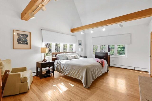 bedroom with vaulted ceiling with beams, rail lighting, light wood-style flooring, and a baseboard heating unit