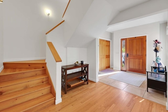 entrance foyer featuring light wood-type flooring, baseboards, lofted ceiling, and stairway
