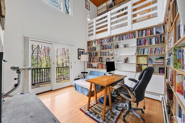 home office featuring a towering ceiling, wood finished floors, and a wealth of natural light