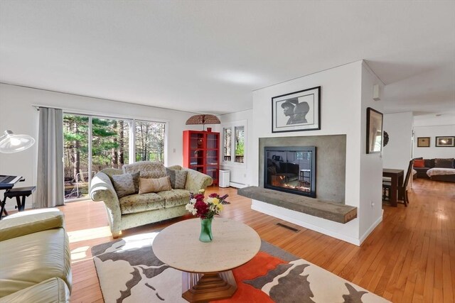 living area with light wood-style floors, a glass covered fireplace, and visible vents