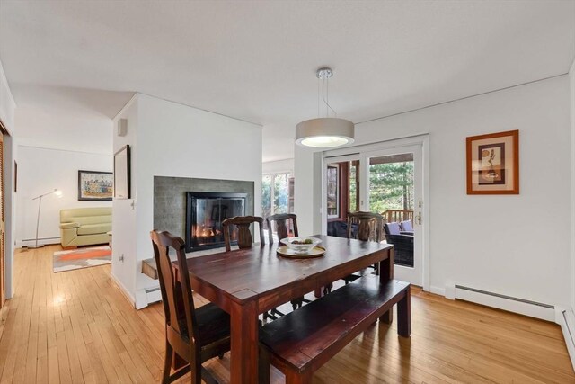 dining space featuring a glass covered fireplace, a baseboard radiator, a baseboard heating unit, and light wood-type flooring