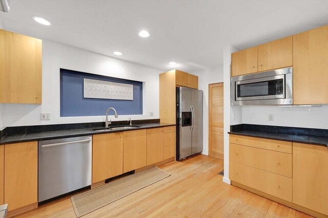 kitchen with a sink, dark countertops, stainless steel appliances, and light wood-style flooring
