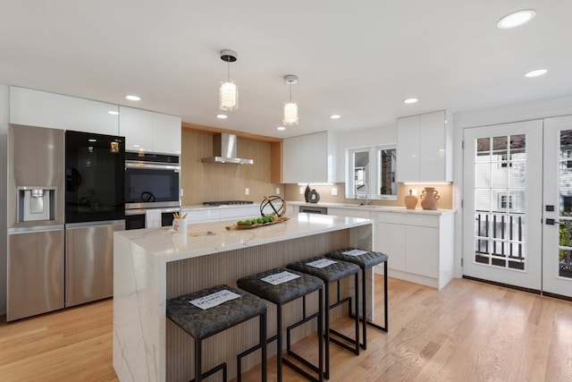 kitchen featuring white cabinets, stainless steel appliances, a kitchen island, and wall chimney range hood