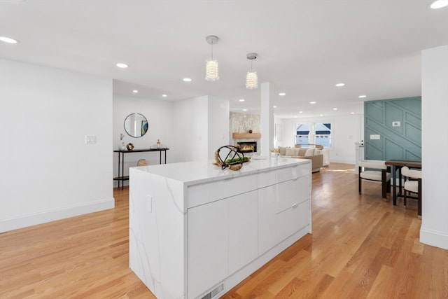 kitchen with white cabinetry, light hardwood / wood-style flooring, a kitchen island, and pendant lighting