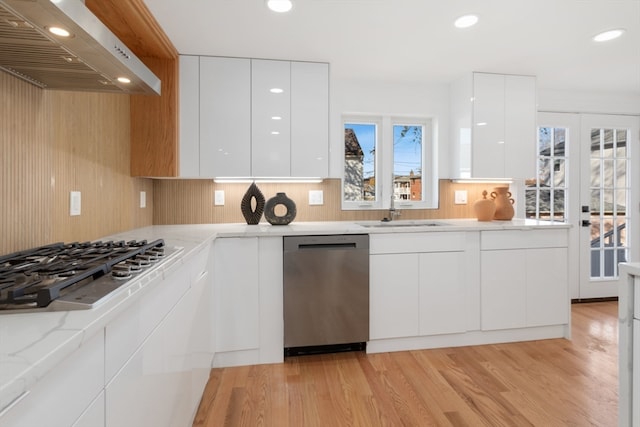 kitchen with light wood-type flooring, stainless steel appliances, white cabinetry, and wall chimney range hood