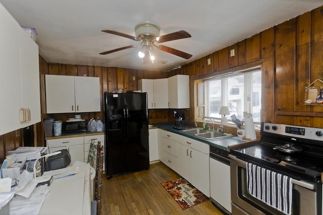 kitchen featuring white cabinets, a sink, wood walls, and black appliances