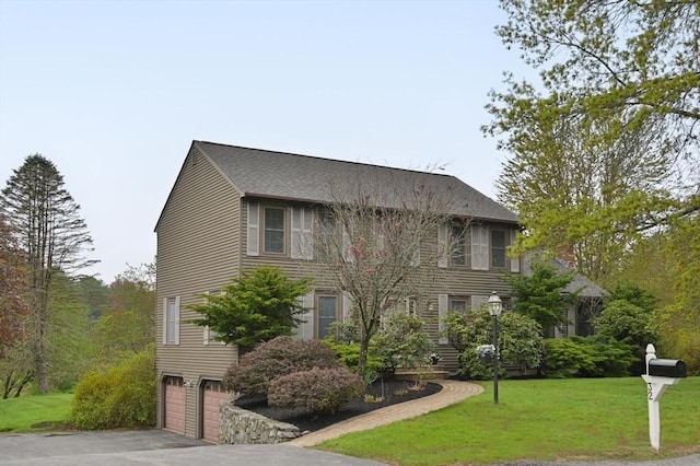 colonial house with an attached garage, a front lawn, driveway, and a shingled roof