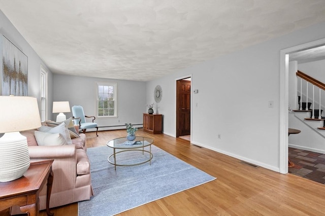 living room featuring stairway, baseboard heating, wood finished floors, and baseboards