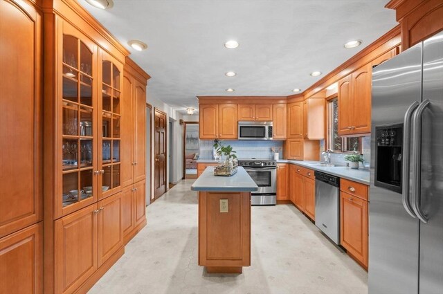 kitchen featuring appliances with stainless steel finishes, a sink, a kitchen island, light flooring, and glass insert cabinets