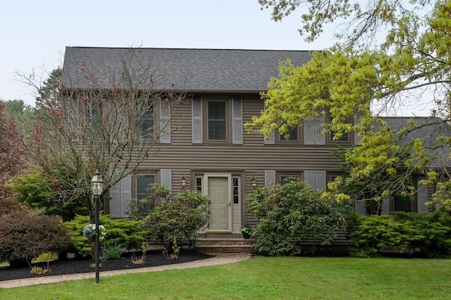 colonial inspired home with a front yard and a shingled roof