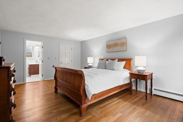 bedroom with wood finished floors, baseboards, a baseboard radiator, and connected bathroom