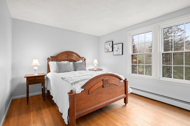 bedroom featuring multiple windows, wood finished floors, a baseboard radiator, and baseboards