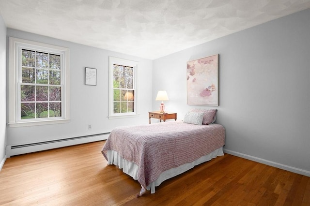 bedroom featuring baseboard heating, wood finished floors, and baseboards