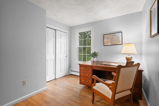 office area with a baseboard heating unit, light wood-type flooring, and baseboards