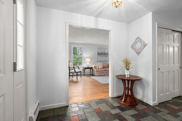 hall with a baseboard radiator, stone tile floors, and baseboards